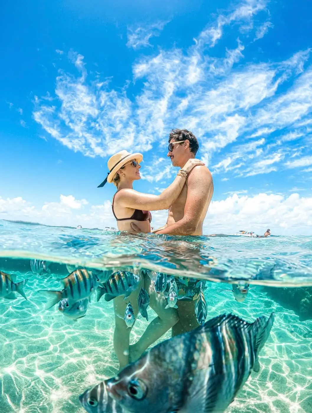 Pareja fotografiada mitad dentro, mitad fuera del agua con peces